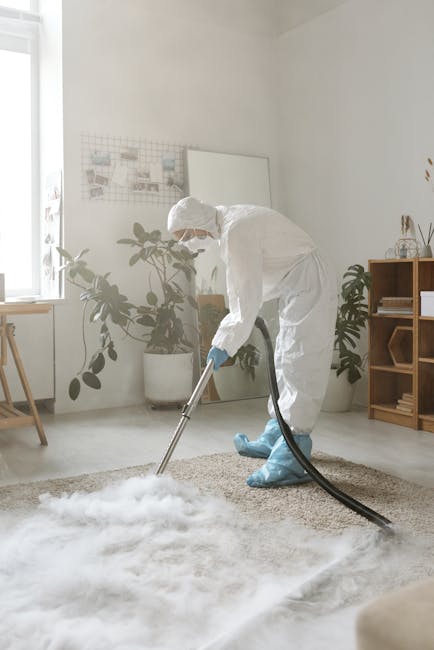 A person holding a yellow portable air mover or blower positioned on a patterned area rug in a room with wooden flooring. The scene shows the close-up of their hands and partly visible head, emphasizi